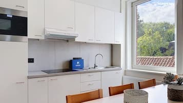 A modern kitchen with white cabinets, a built-in oven, a stainless steel range hood, and a window with a view of greenery.