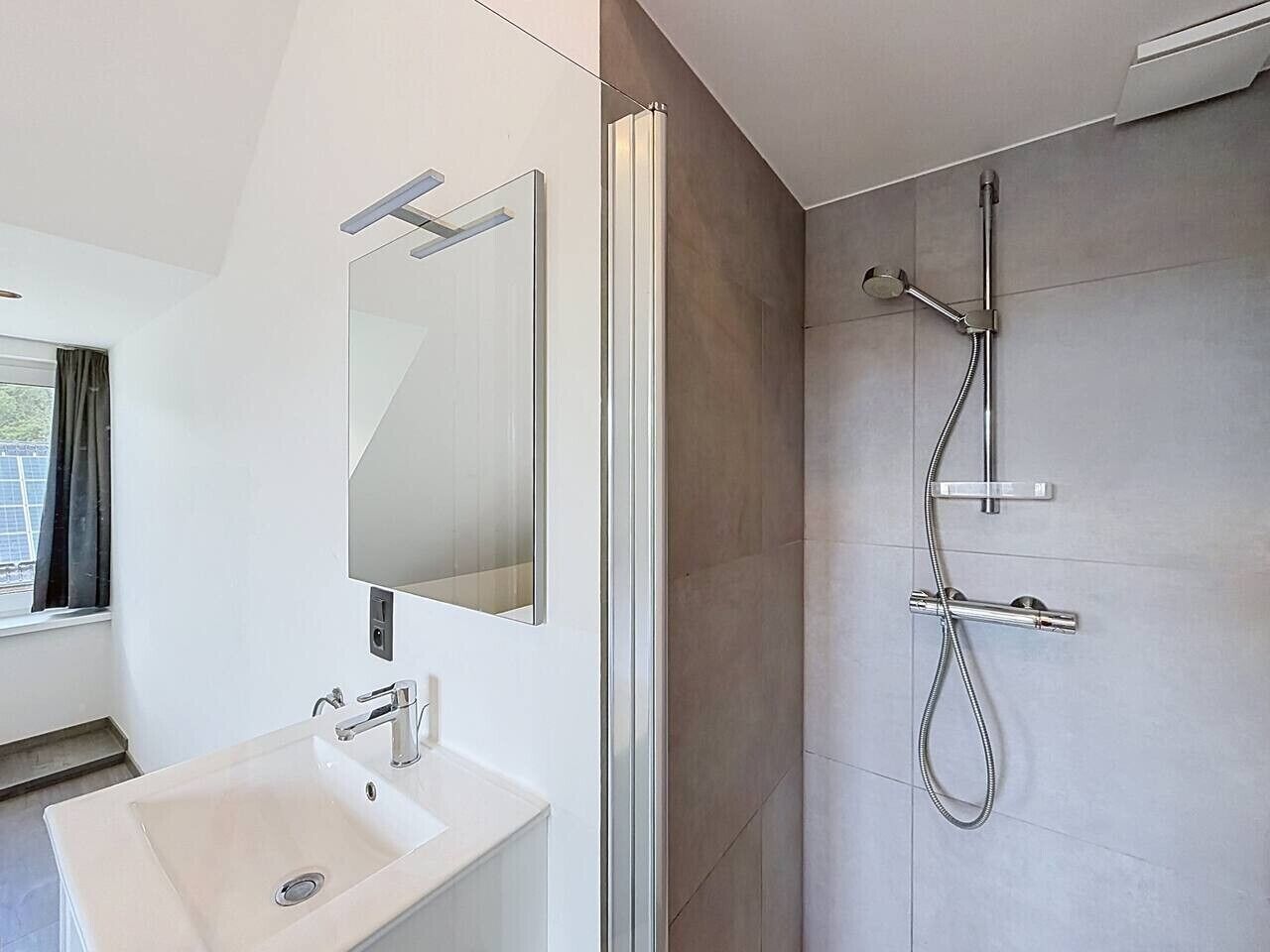 Un bagno moderno con uno specchio grande, un lavandino e una doccia.