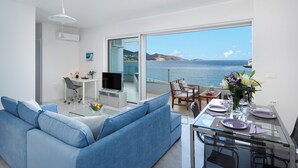 Una sala de estar moderna con un sofá, una mesa de comedor de vidrio, un televisor y vista al mar.