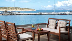 Una mesa de madera con una jarra de vidrio y fruta, dos sillas de madera, y vista al mar y tierra distante.