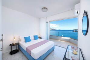 Ein Schlafzimmer mit einem großen Bett, einem Nachttisch, einem Glastisch und Blick aufs Meer.