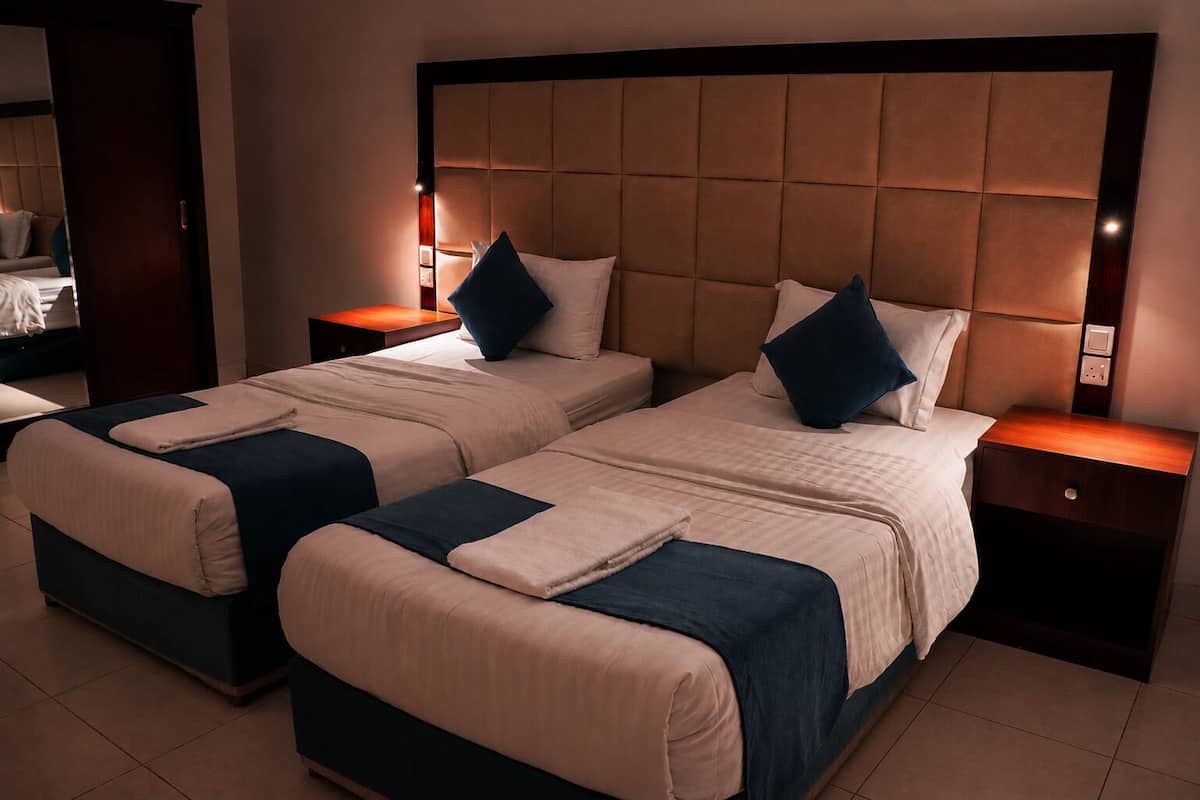 Habitación de hotel con dos camas, cabecero de madera, mesitas de noche y un espejo.