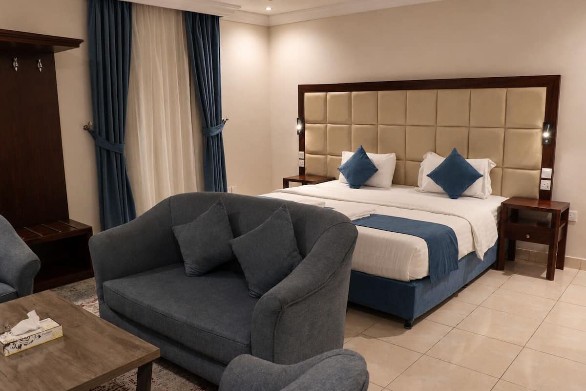 A hotel room with a bed, a grey sofa, a wooden nightstand, and a wooden wardrobe.