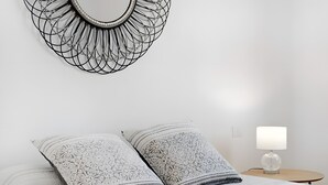 Een net opgemaakt bed met gekleurde kussens, een wanddecoratie met abstracte kunst, en een nachtkastje met een lamp.