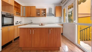 Een moderne keuken met houten kastjes, een centraal eiland en een raam met een gele luifel.