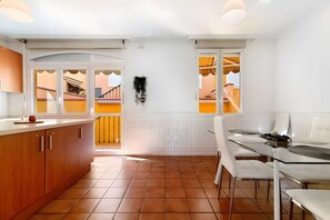 A modern kitchen with a dining area, white walls, and a view through a glass door.