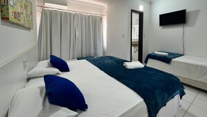 Ein Hotelzimmer mit zwei Betten, einem Fernseher, einem Badezimmer und einem Fenster mit Vorhängen.