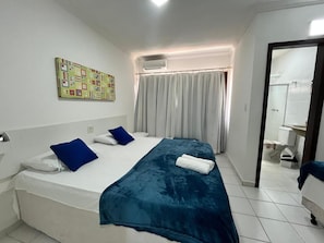 A bedroom with a bed, a window with curtains, an air conditioning unit, and a bathroom visible through an open door. - Dwelling place of Israel, Revelation 30 (Porto Seguro)