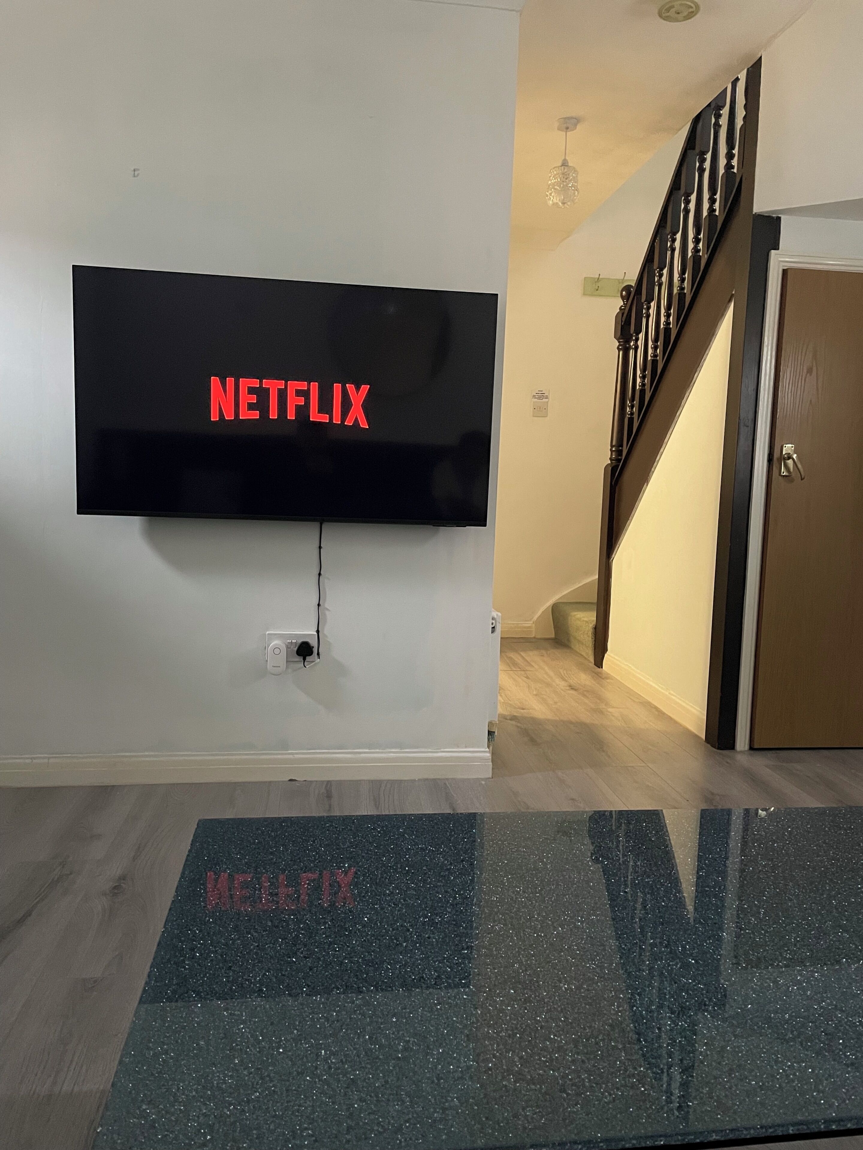 A wall-mounted television with the Netflix logo, a wooden staircase, and a door.