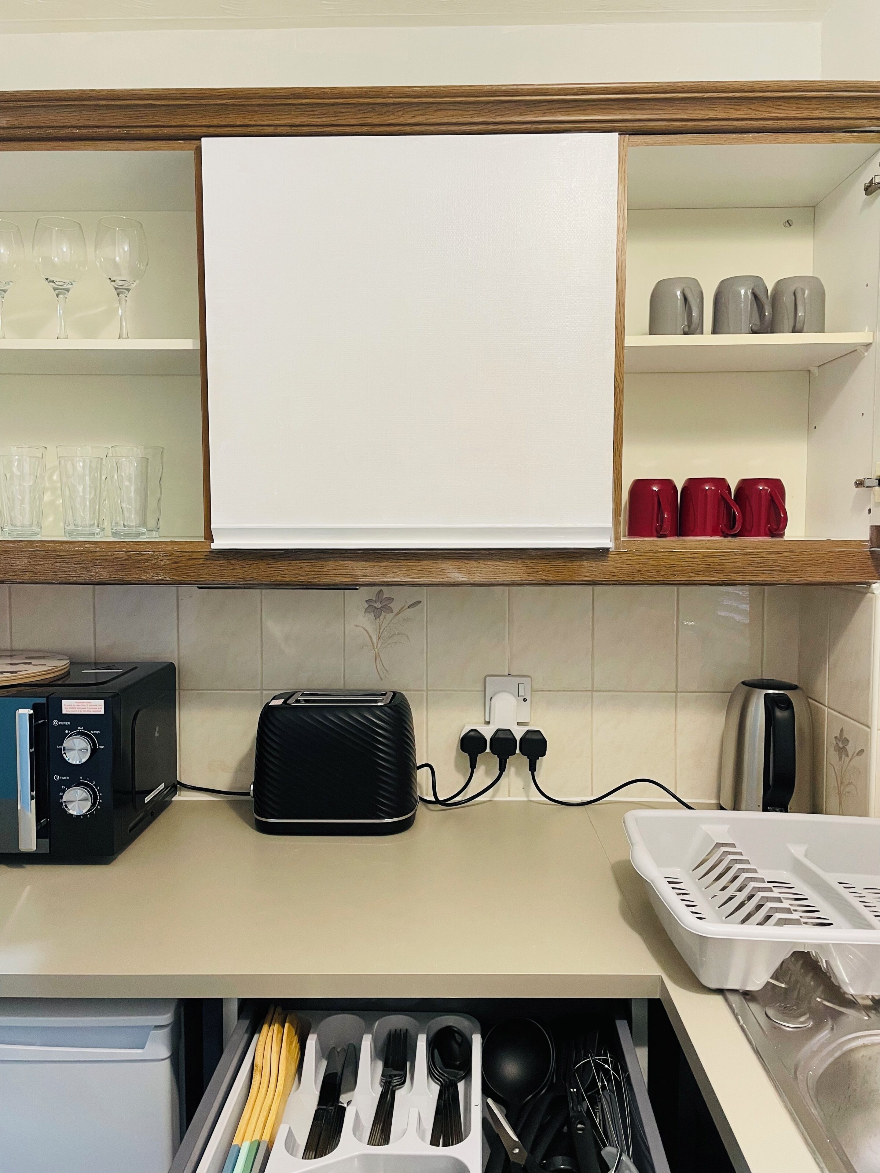 A kitchen with a toaster, a kettle, and a drawer with utensils.