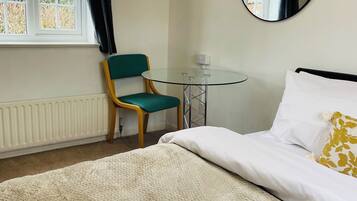 A hotel room with a bed, a chair, a round mirror, and a window with curtains.