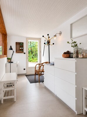 Eine moderne Küche mit weißen Schränken, einem Holzbstuhl, einer schwarzen Stehlampe und Blick ins Grüne.