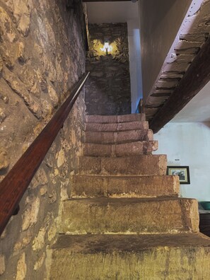 Eine Treppe mit Steinstufen und Holzläufingen, die zu einem Raum mit einer Steinwand und einer Lampe führt.