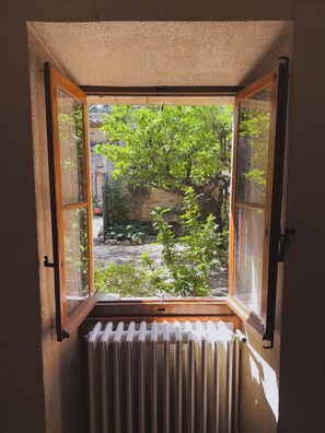 Ein offenes Fenster mit Blick auf einen Garten und eine Steinmauer.