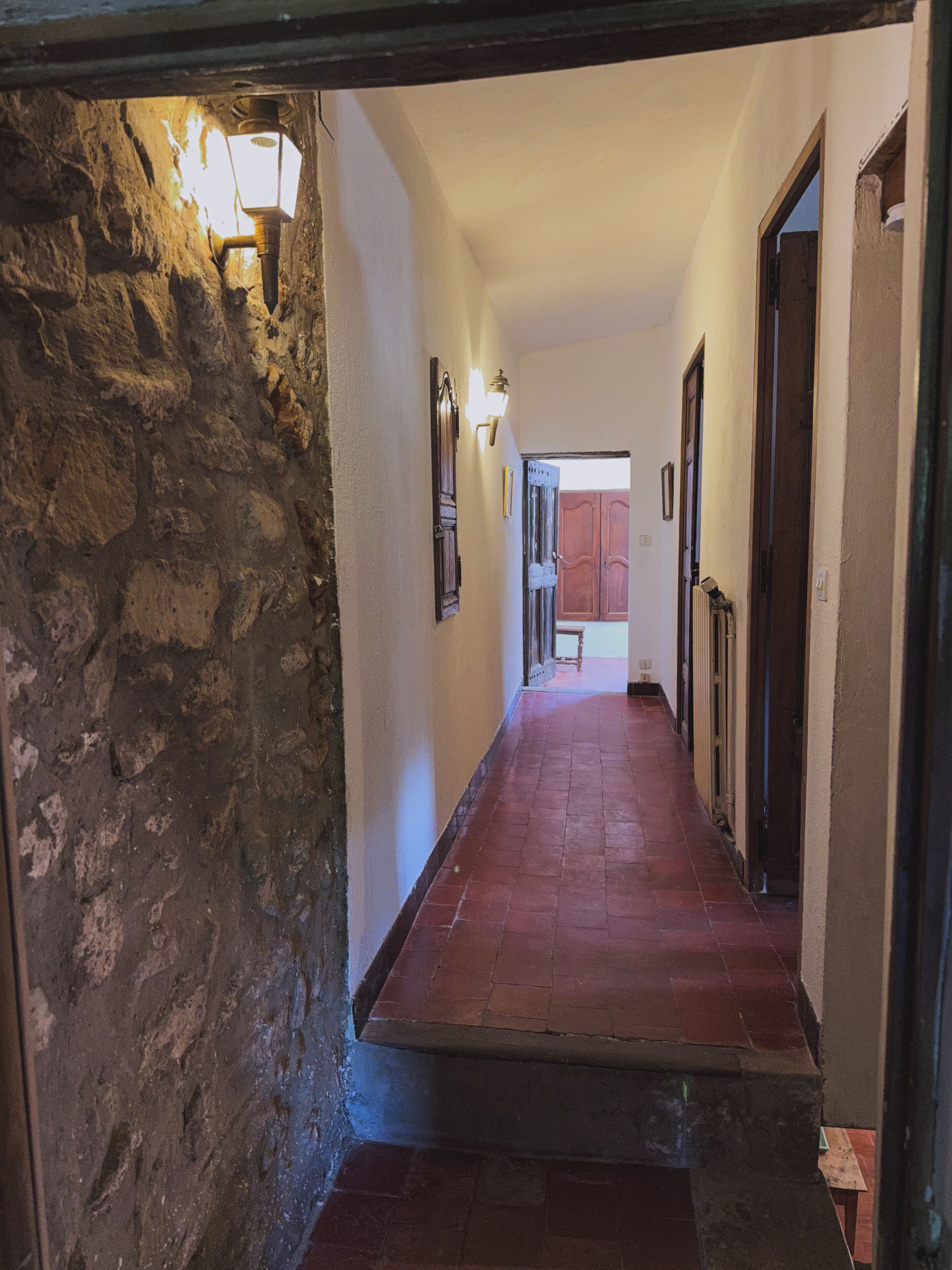 A hallway with a stone wall on one side, a wooden floor, and a door at the end.