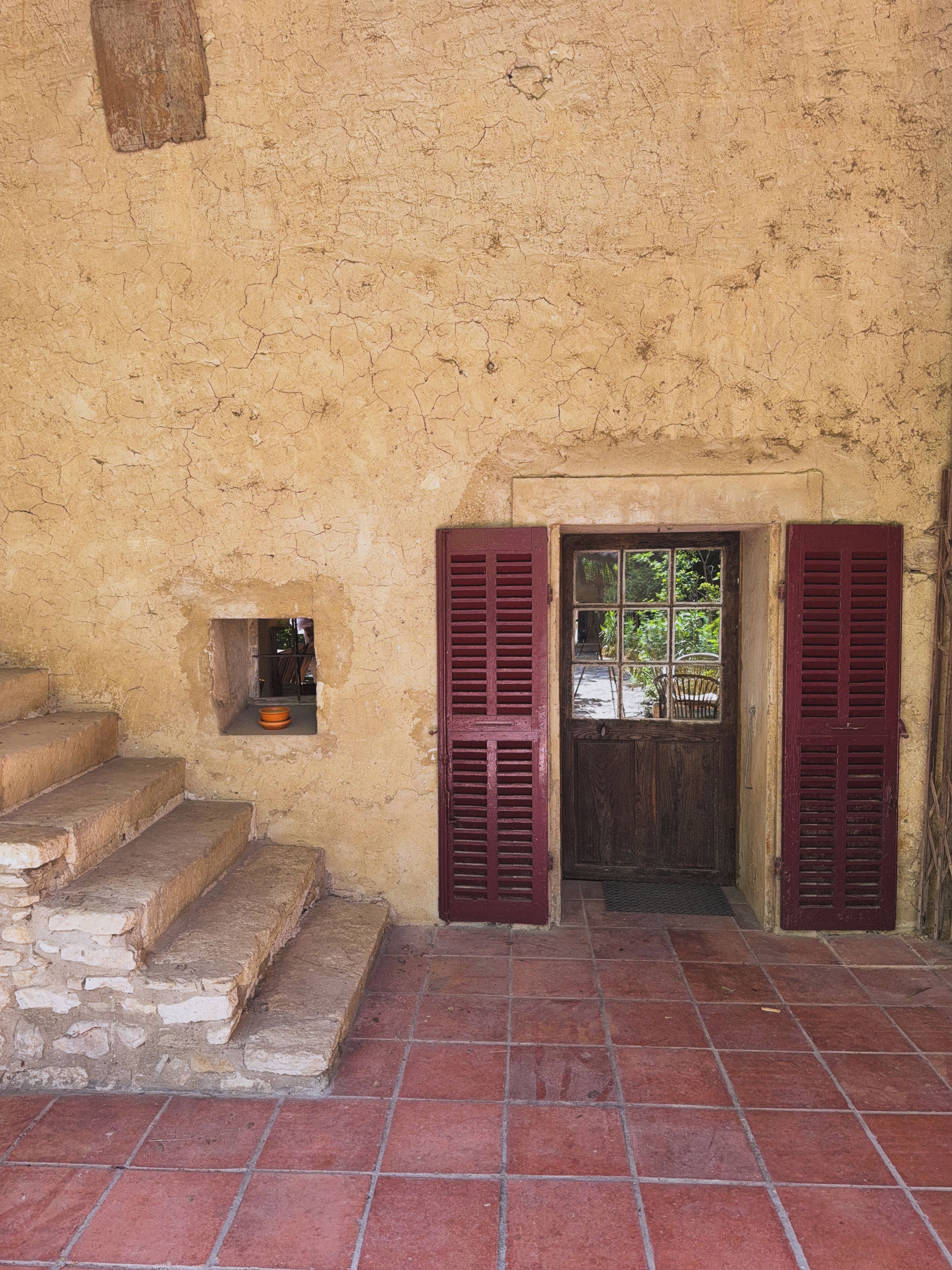 A rustic building with a set of stone steps leading to a door with wooden shutters.