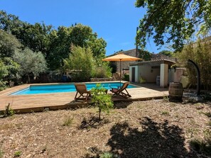 Une piscine avec une terrasse en bois, des chaises longues et un parasol.