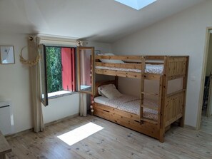 Una habitación con una cama litera, una ventana con cortinas, un escritorio pequeño y un tragaluz.