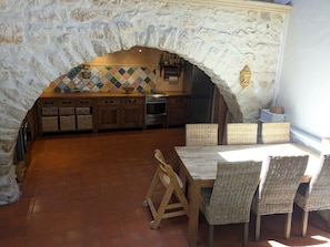 A stone archway leading to a kitchen with wooden cabinets, a tiled backsplash, and wicker furniture.