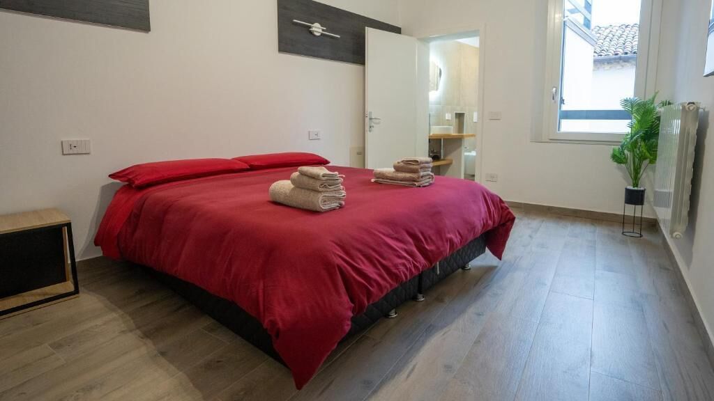 Un dormitorio con cama, una colcha roja y toallas dobladas.