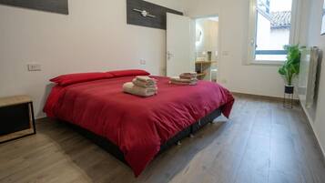 Un dormitorio con cama, una colcha roja y toallas dobladas.