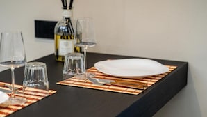 Una mesa de comedor dispuesta con copas de vino, una botella de vino y un plato blanco sobre una mesa negra con un mantel individual a rayas.