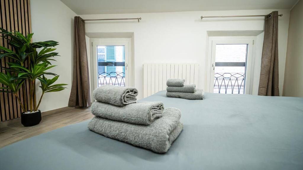 A hotel room with a large bed, two windows, a radiator, and a potted plant.