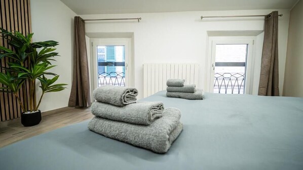 A hotel room with a large bed, two windows, a radiator, and a potted plant. - ESTENSIA Room&Suite (Ferrara)