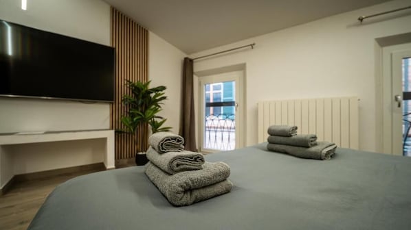 Et moderne hotelværelse med et fladskærms-TV, en potteplante, en stor seng med gråt sengetøj og udsigt udad.