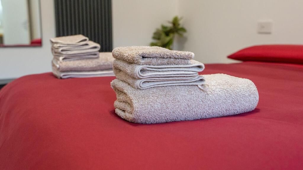 Un lit bien fait, avec une couverture rouge et une pile de serviettes pliées.