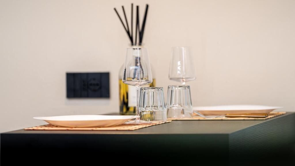 A dining table with a bottle, glasses, and a plate set on a mat.