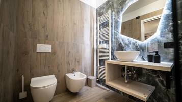 Un bagno moderno con pavimento in legno, un bidet, un lavandino con schienale in marmo e uno specchio.