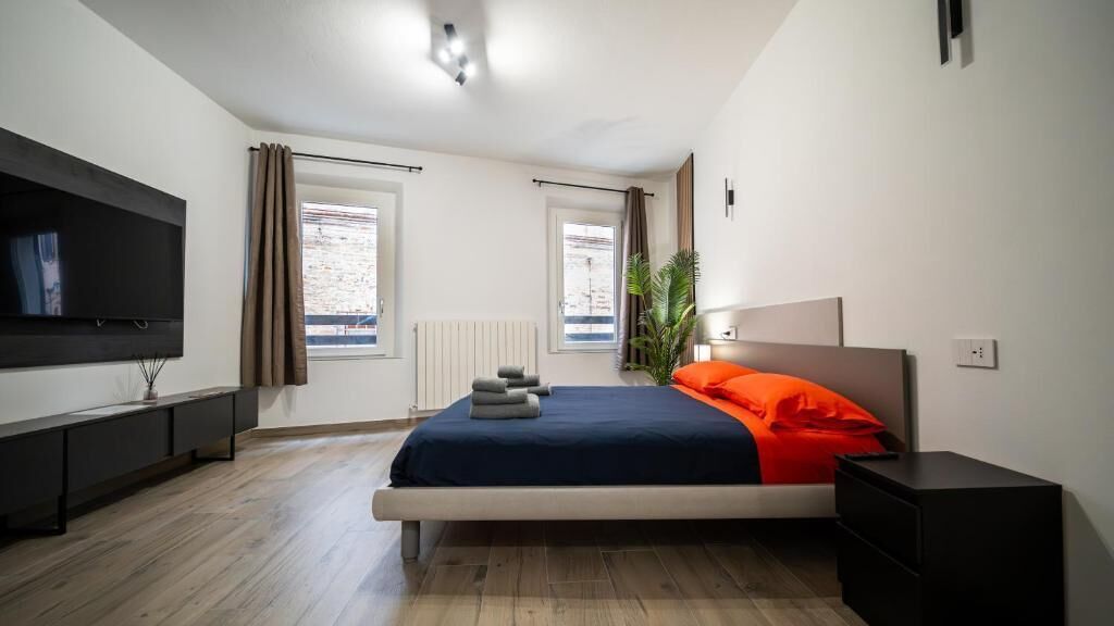 Un dormitorio con cama, televisor, radiador y ventanas.