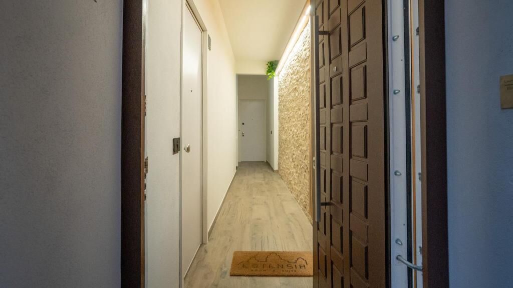 A narrow hallway with a wooden floor, a doormat, and a door with a metal handle.