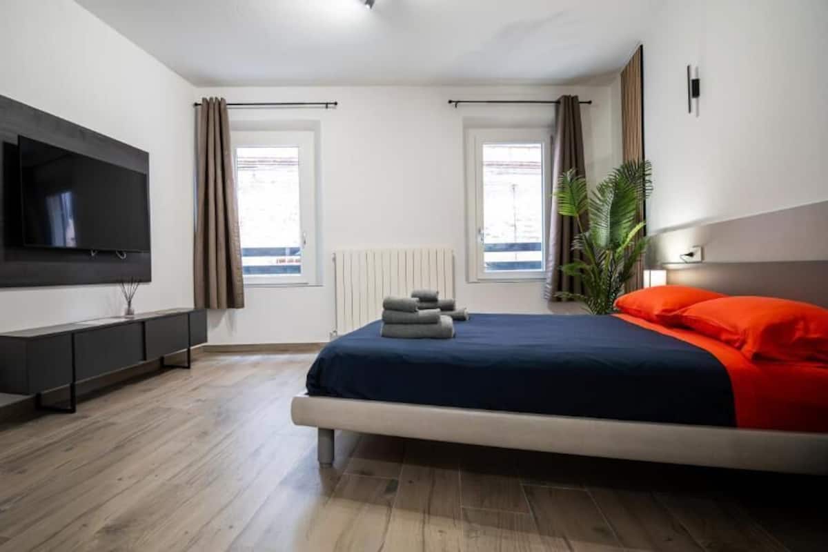 A modern bedroom with a bed, TV, and a plant.
