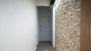 A narrow hallway with a white door at the end, a stone wall on one side, and a wooden panel on the other.