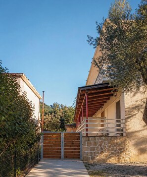 Un bâtiment en pierre avec un portail en bois, un balcon doté d’une rambarde rouge et un ciel dégagé.