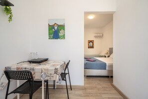 Ein Zimmer mit einem Bett, einem Tisch mit Stühlen, einem Bild an der Wand und einem kleinen Fenster.
