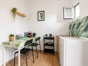 Une cuisine compacte comprenant un coin repas, un réfrigérateur, un évier et une petite étagère avec des plantes.