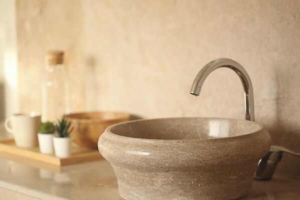 A stone sink with a curved faucet, a glass bottle, and a small potted plant on a wooden tray.