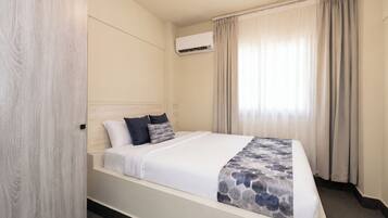 Una camera d'albergo con un letto, una finestra con tende, un condizionatore d'aria e una parete in legno.