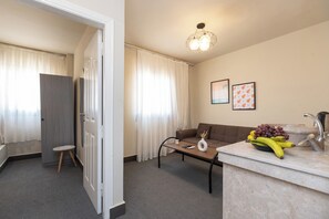 A modern hotel room with a sofa, a coffee table, a small stool, a fruit bowl, and a sink with a faucet.