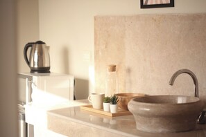 Una cucina con un lavandino, un bollitore, un vassoio di legno e una piccola pianta.
