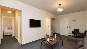 A modern living room with a sofa, a coffee table, and a flat-screen TV mounted on the wall. There are two doors leading to other rooms, and a small table with a vase and candle. - Seven Stays Sidi Abd El-Rahman (El Alamein)
