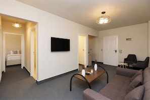 A modern living room with a sofa, a coffee table, and a flat-screen TV mounted on the wall. There are two doors leading to other rooms, and a small table with a vase and candle. - Seven Stays Sidi Abd El-Rahman (El Alamein)