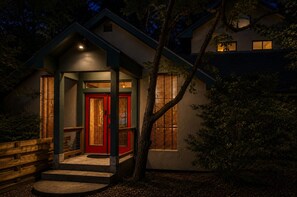 Una casa con puerta roja, un pequeño porche y un árbol en el frente.