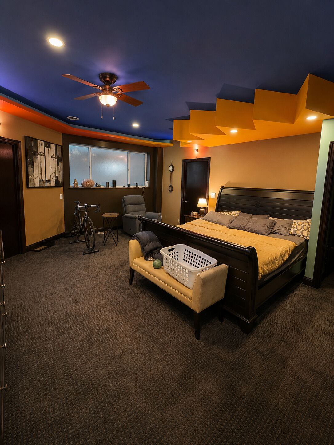 A bedroom with a bed, a ceiling fan, a window, a bicycle, and a laundry basket.