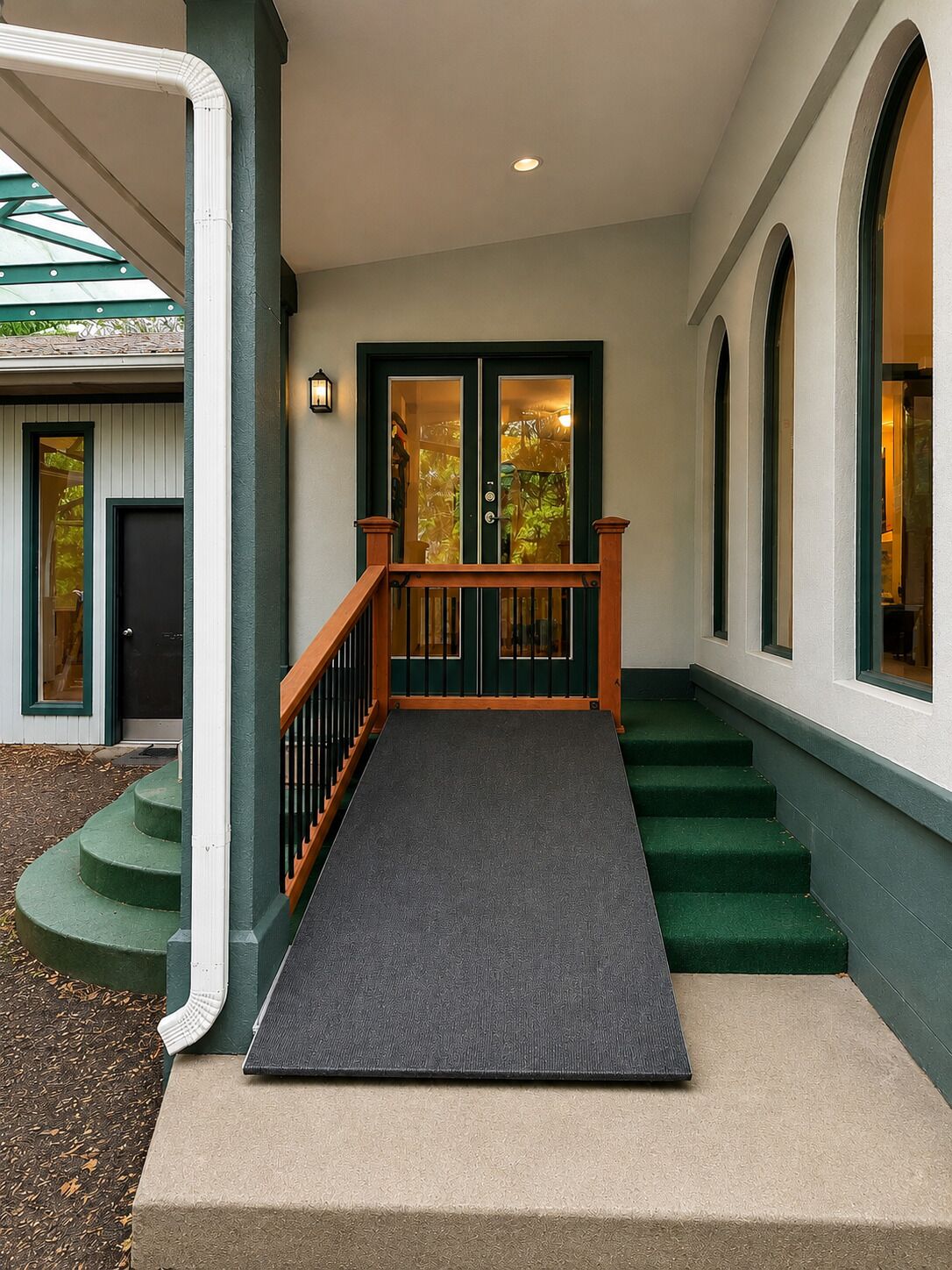 A building entrance with a ramp leading to a set of stairs, a door with glass panels, and a light fixture above the door.