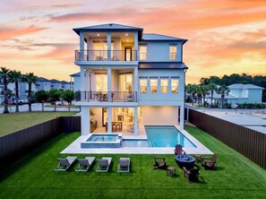 Une maison à deux étages avec une piscine, un espace salon extérieur et une vue sur le coucher de soleil.