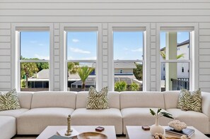 A modern living room with a beige sectional sofa, a coffee table, and a large window with a view of a residential area.
